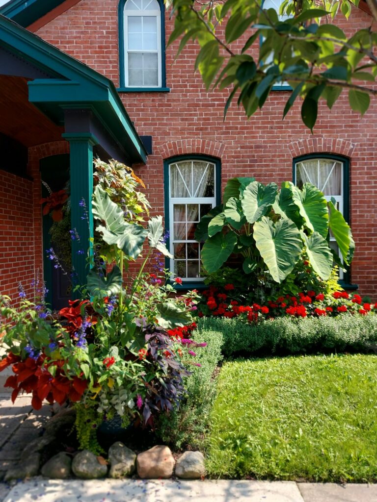Homeowner cleaning a front walkway beside trimmed shrubs, fresh mulch, and a neatly painted entry door.