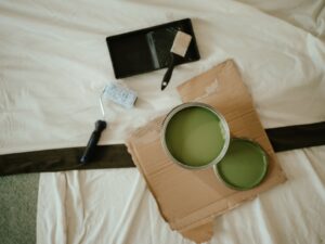 A person holds up paint swatches against a light-filled living room wall with natural wood trim.